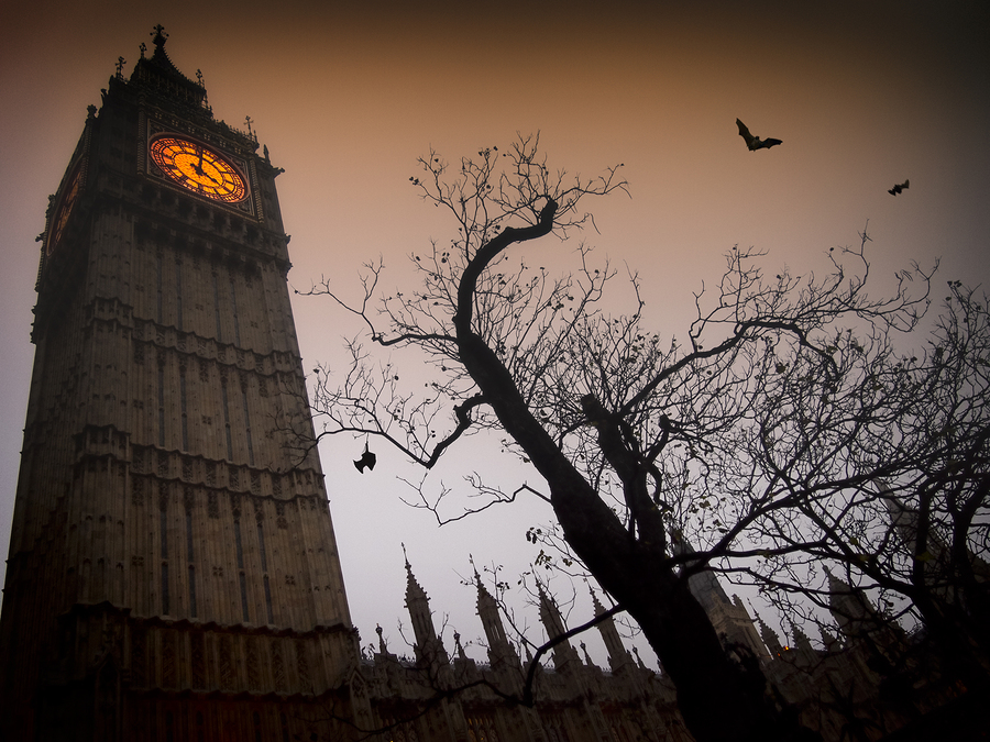 The spooky clock tower of Westminster with a bare tree and flying bats