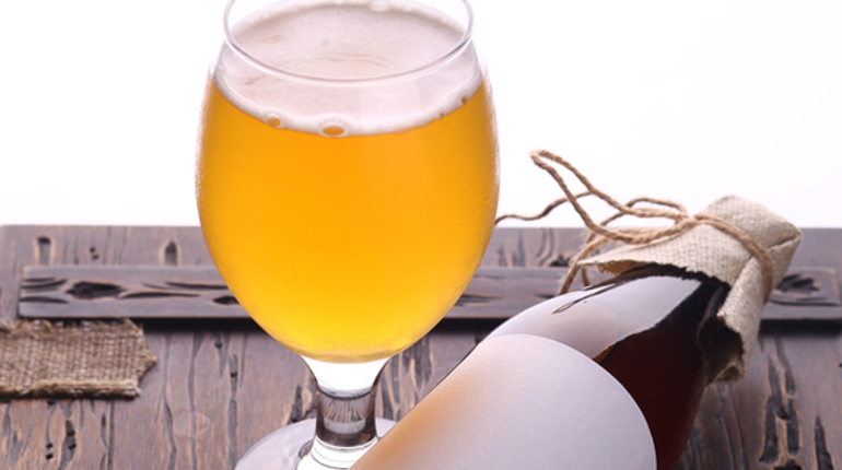 Bottle with blank label template and glass of home brewed craft beer standing on a wooden chest with bright white background