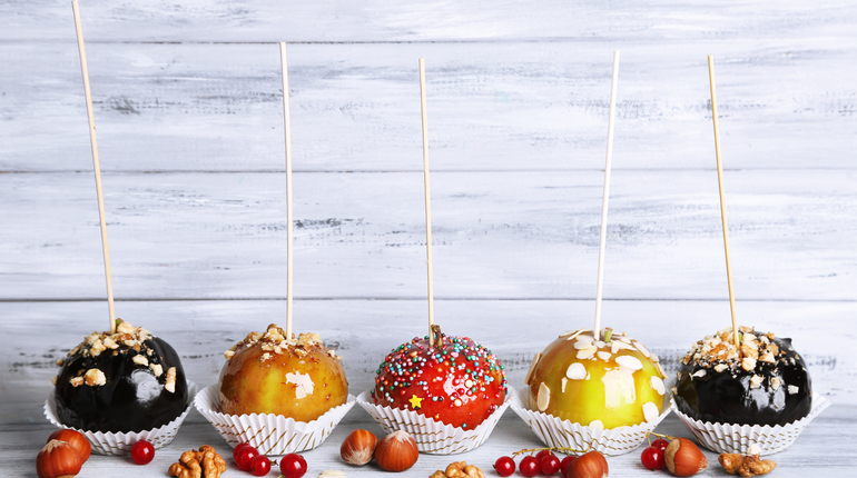 Sweet caramel apples on sticks with berries, on wooden table