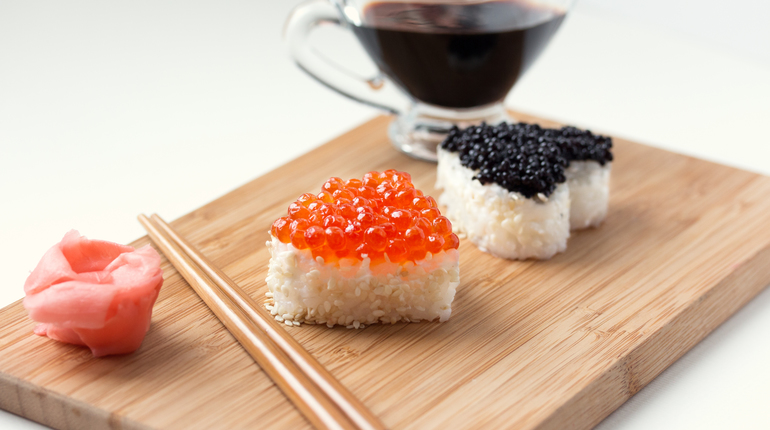 Two heart shaped sushi with salmon roe and beluga caviar on wooden desk. ginger, chopsticks and soy sauce.